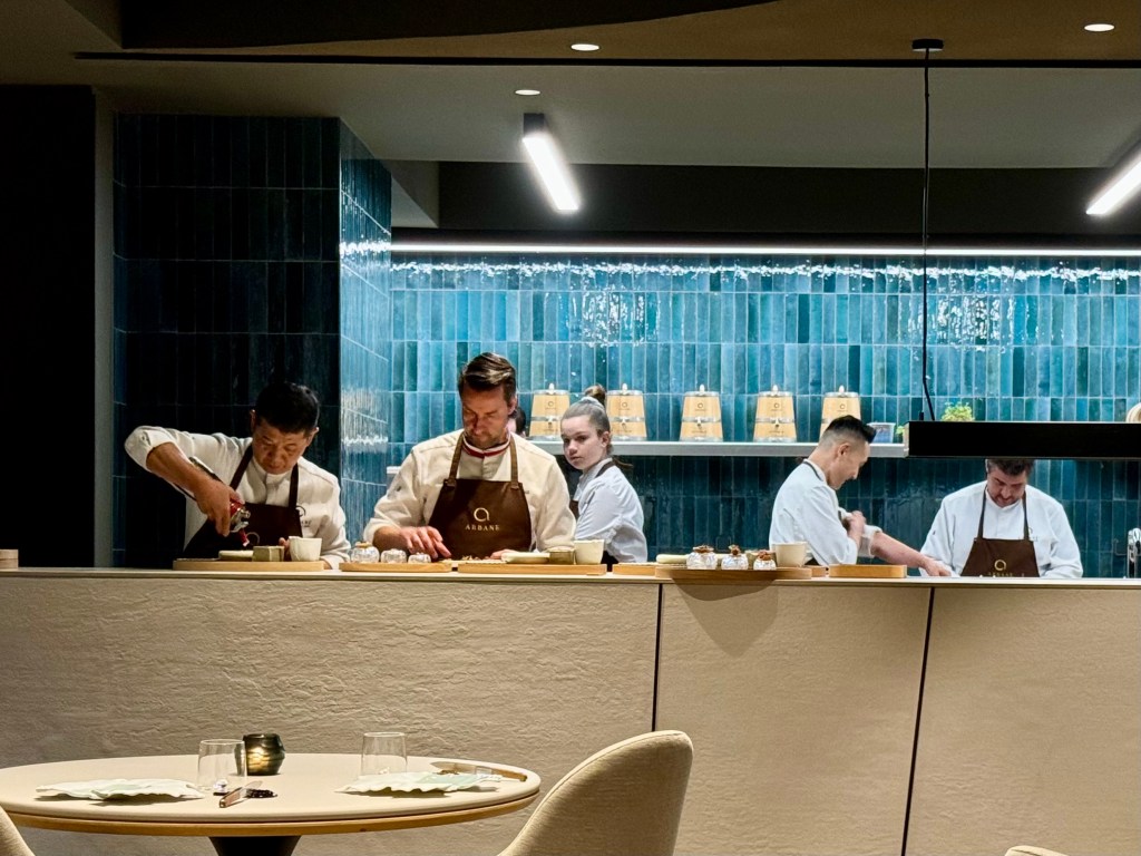 Chefs preparing dishes in a modern kitchen with blue tiles and a clean aesthetic.